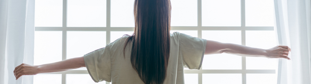 女性がカーテンを開けて光を浴びている
