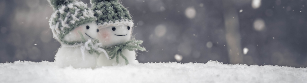 雪が降っている外で緑のニット帽を被った小さい雪だるま2体