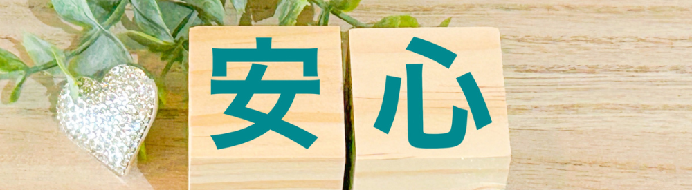 “安心”の文字が木製ブロックに記された画像。緑の葉とハートモチーフが添えられ、信頼感と安心感を演出するビジュアル。