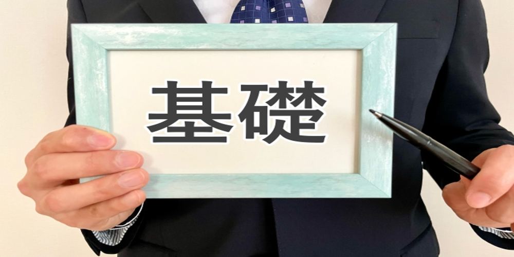 “基礎”と書かれたフレームを手に持ち、ペンで示すスーツ姿
