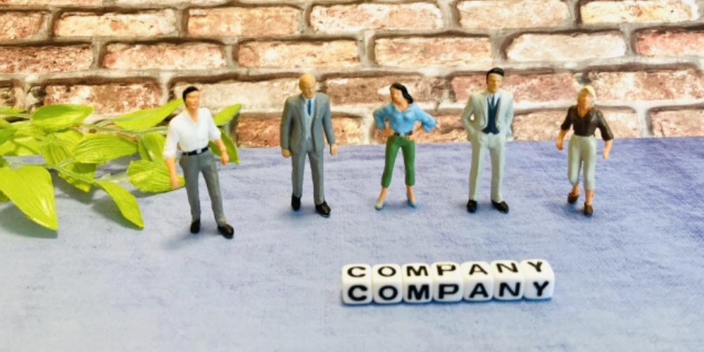 「レンガの背景の前に立つ5人のビジネスフィギュアと『COMPANY』の文字が書かれたサイコロ型ブロック」
