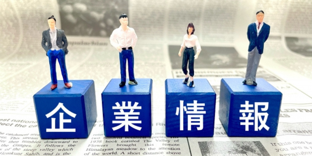 企業情報の文字が書かれた青いブロックとその上に立つ4人のビジネスマン
