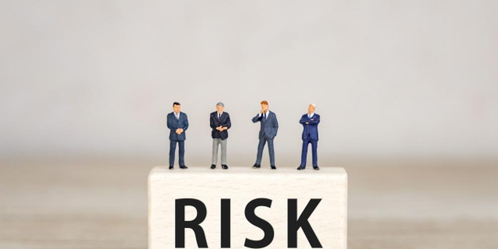 「RISK」の文字が書かれた木ブロックの上に立つ4人