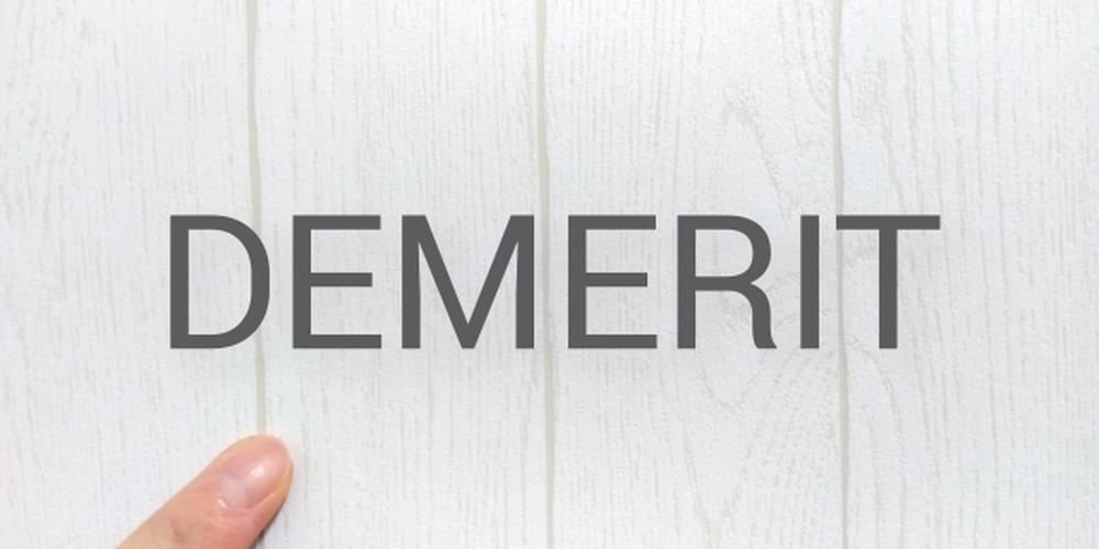 白い木目調の背景に「DEMERIT」と書かれ、左下に指差しの指が写っているシンプルな画像