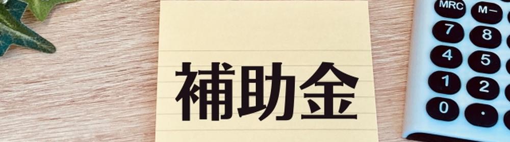 補助金と書かれたメモ、ペンと電卓が添えられたデスク。補助金制度や財務サポートの案内を示すイメージ
