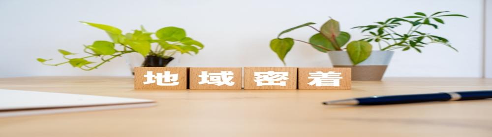 木製ブロックに『地域密着』の文字が並ぶデスク上の風景。地域に根ざしたサービス提供を象徴