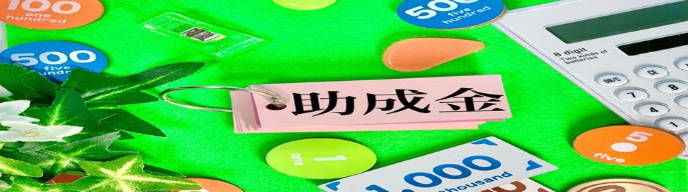 助成金と書かれた単語カードと電卓、お金のパーツが並ぶカラフルな構成。中小企業向けの支援制度を示すイメージ