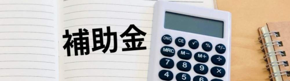 補助金の文字と電卓、ノートが置かれたデスクのイメージ