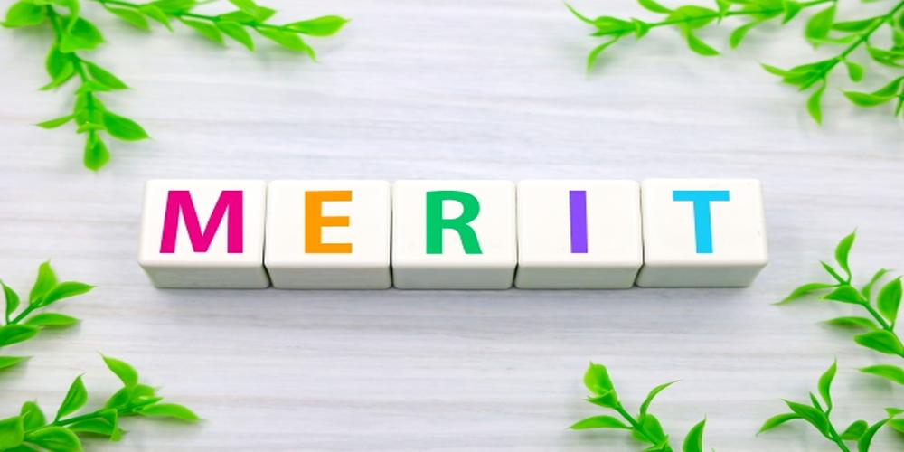 “MERIT”の文字がカラフルなブロックで並べられ、植物で囲まれた明るいイメージ。企業やサービスの利点・強みを象徴するビジュアル。
