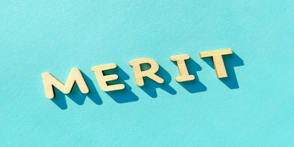 “MERIT”の文字が木製のブロックで並べられ、青い背景に影