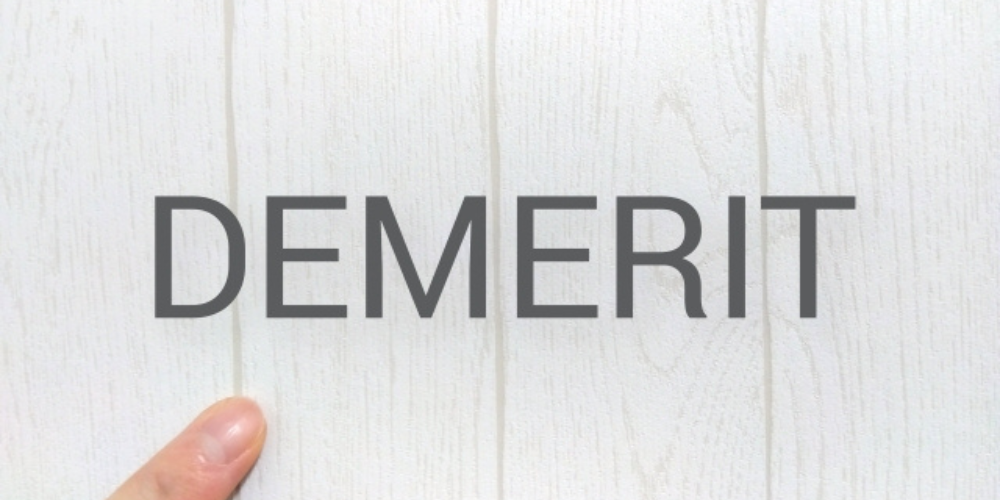 白い木目背景に『DEMERIT』の文字と指先