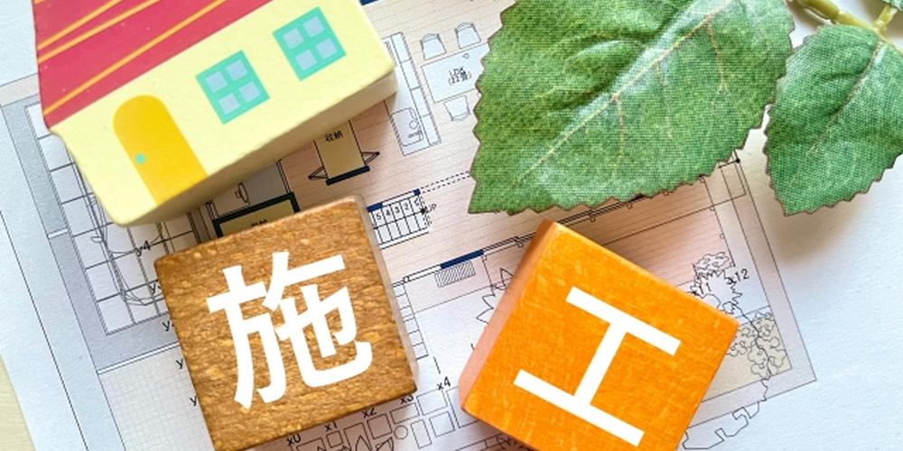 住宅模型と設計図の上に置かれた「施工」の文字ブロックと葉