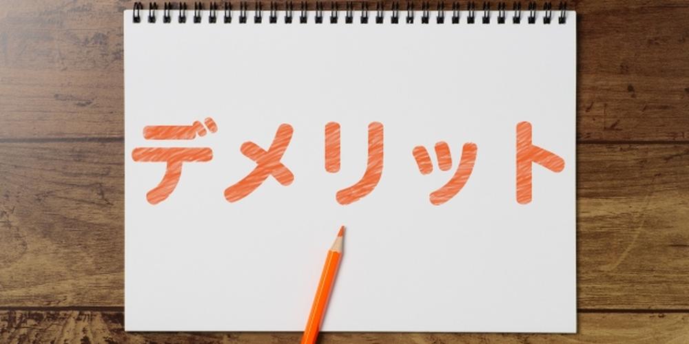 「デメリット」と書かれたノートにオレンジの色鉛筆が添えられている画像