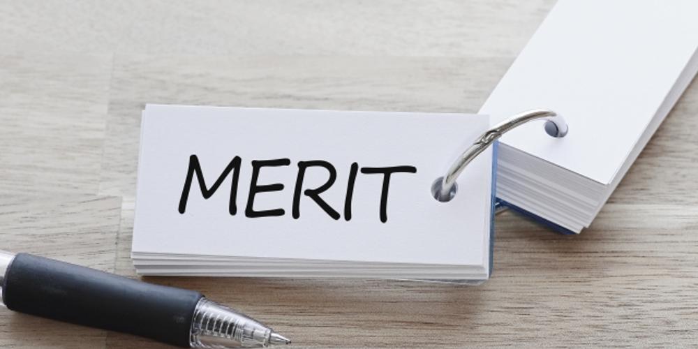“MERIT”と書かれたリング式の単語カードとペンが並ぶ木目調の背景。ビジネスにおける利点や要点整理を示すビジュアル。