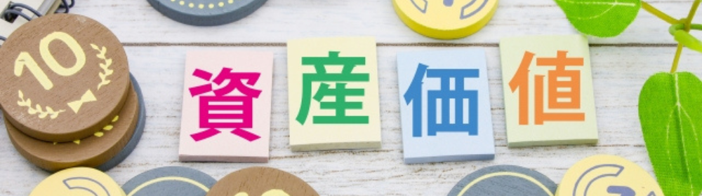 「カラフルな文字で『資産価値』と書かれたブロックと、周囲に配置された木製コインと葉」