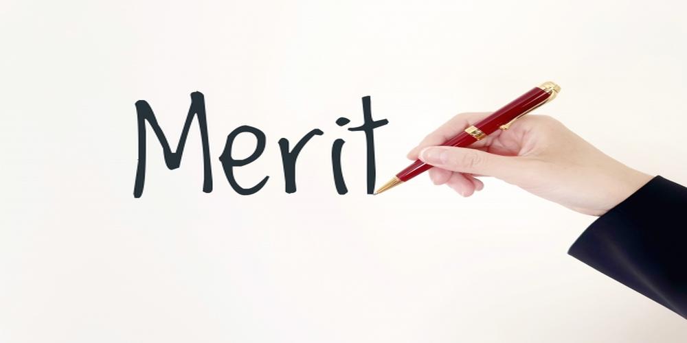 “Merit”の文字を赤いペンで書くビジネススーツの手元