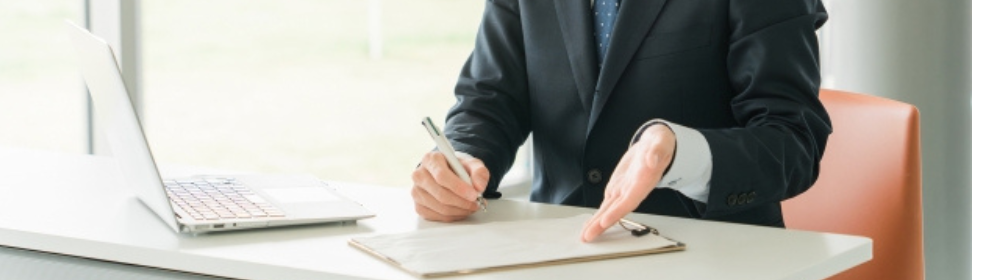 ビジネススーツを着た人物がデスクで資料を前に説明をしている様子