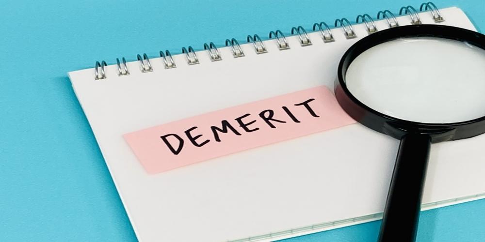 DEMERIT”の文字が書かれた付箋と虫眼鏡が置かれたメモ帳