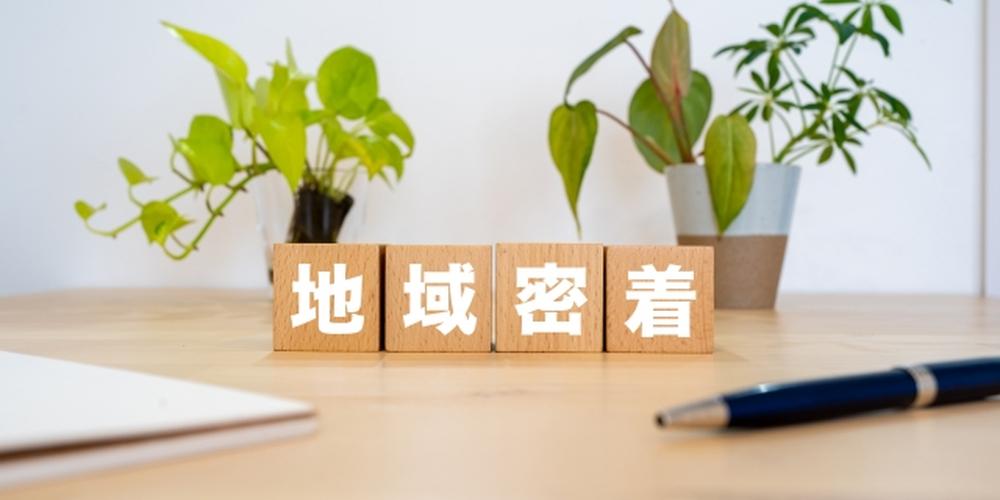 木製ブロックに「地域密着」と書かれた文字と観葉植物が並ぶ、明るくナチュラルな雰囲気のデスク風景