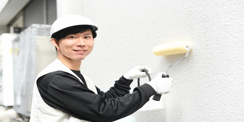 塗装作業中の作業員が笑顔でカメラを見るシーン。清潔感のあるユニフォームと丁寧な作業風景が信頼と安心感を演出するイメージ。