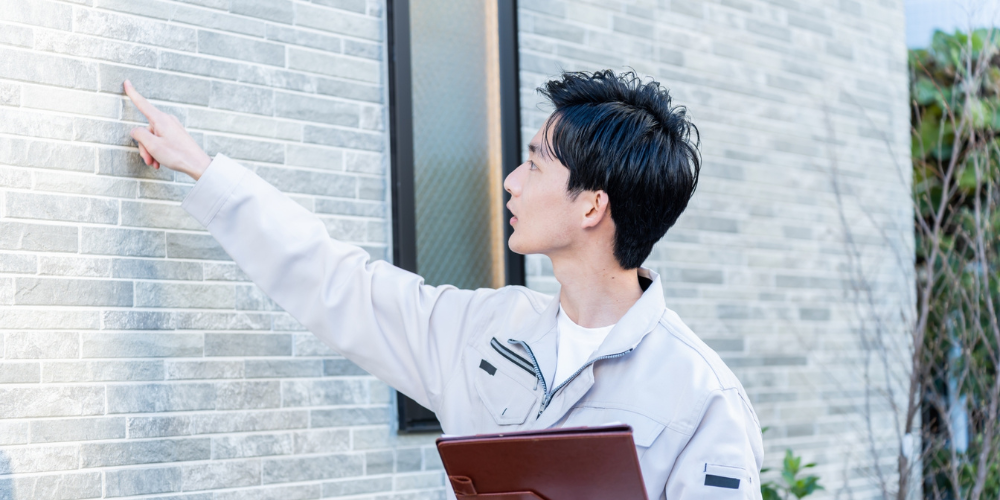 外壁を指差しながら点検する建築技術者