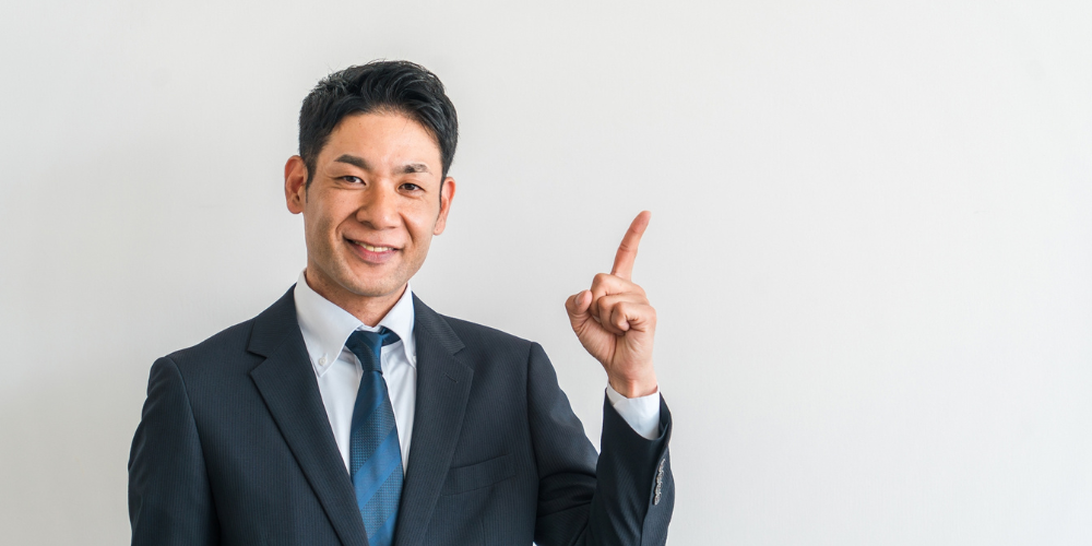 スーツ姿の男性が上を指差すポーズ