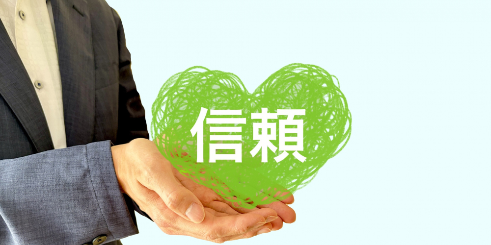 「信頼」と書かれた緑のハートを手に乗せるビジネスマン